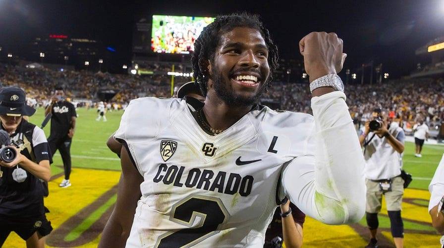 Shedeur Sanders smiling and celebrating after a football game, wearing a Colorado uniform.