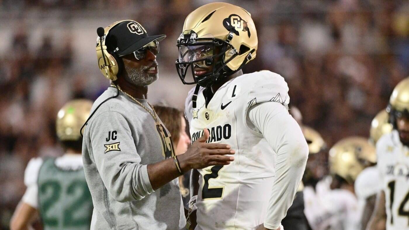 A football coach speaking with a player on the sidelines during a game.