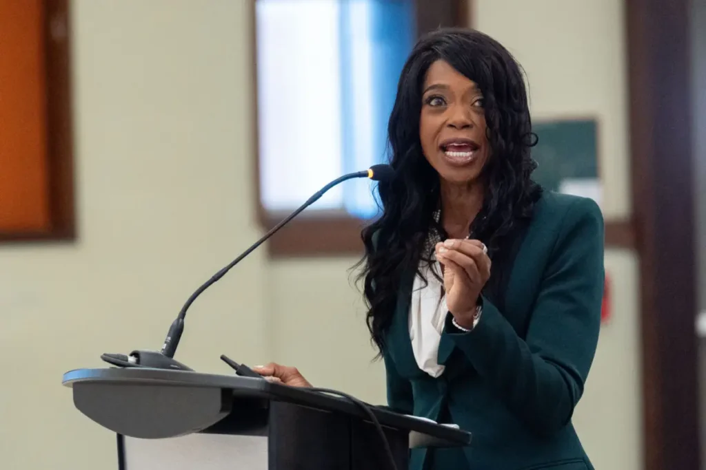 Marva Johnson delivering a speech at a podium with a microphone in a formal setting.