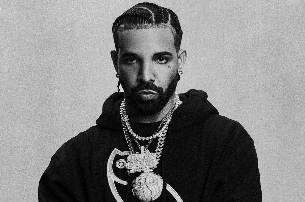 Black and white portrait of a man with braided hair wearing a hoodie and multiple chains.