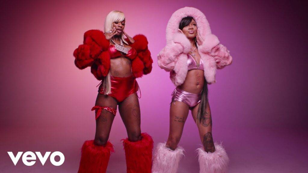 Two women wearing colorful fur outfits and high boots posing against a gradient background.