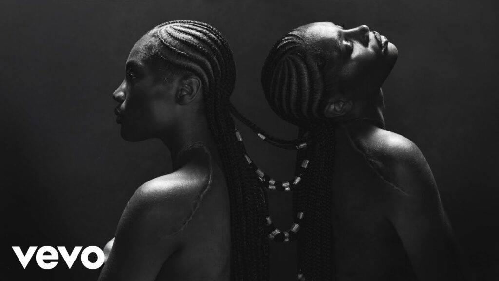 Black and white portrait of two women with braided hairstyles, positioned back to back.