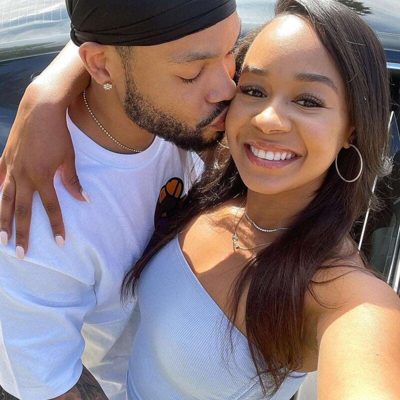 A man kissing a woman on the cheek while they take a selfie together outdoors.