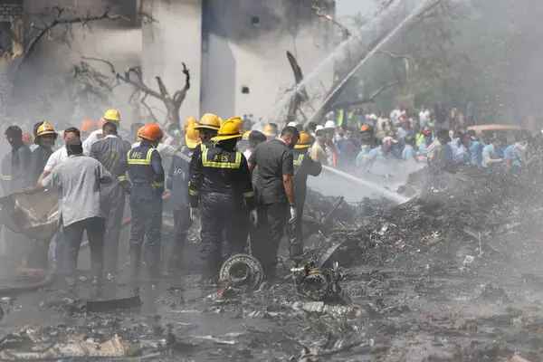 Emergency responders and personnel working at the site of an aircraft crash with smoke and debris visible.