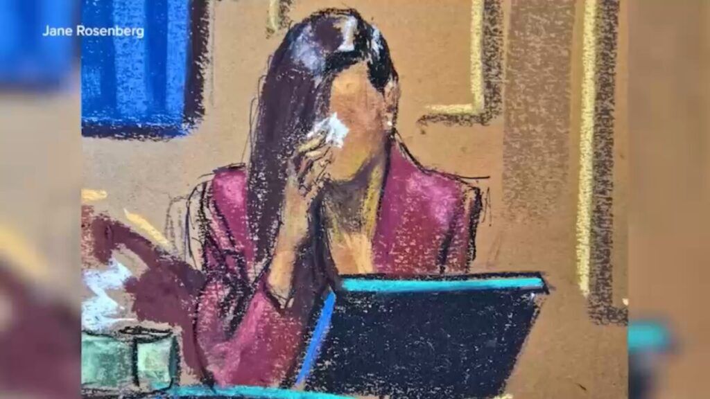 Courtroom sketch of a woman in a red jacket sitting at a computer, appearing to wipe her face.