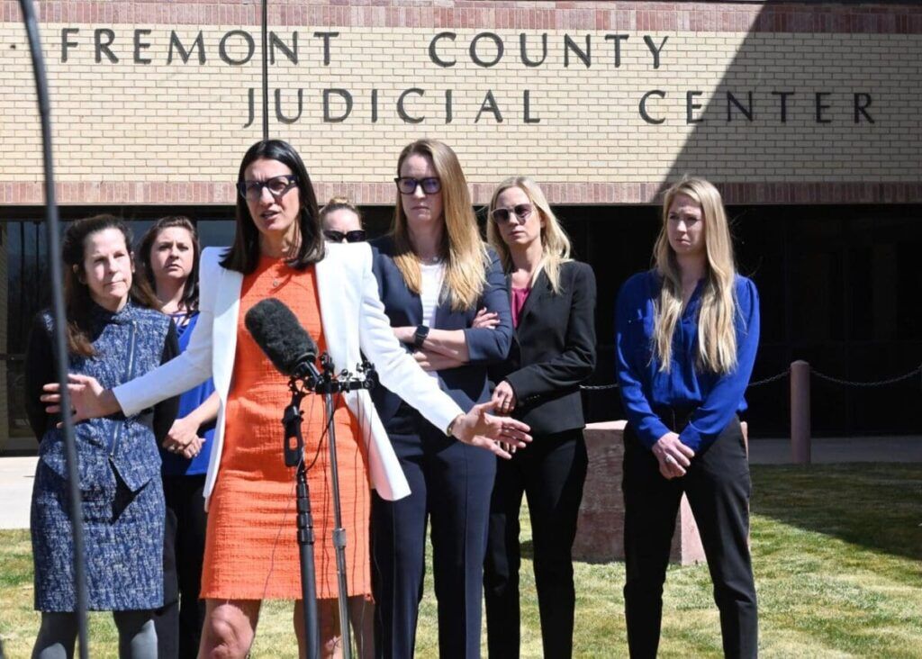 A group of women at a press conference outside the Fremont County Judicial Center, with one woman speaking into a microphone.