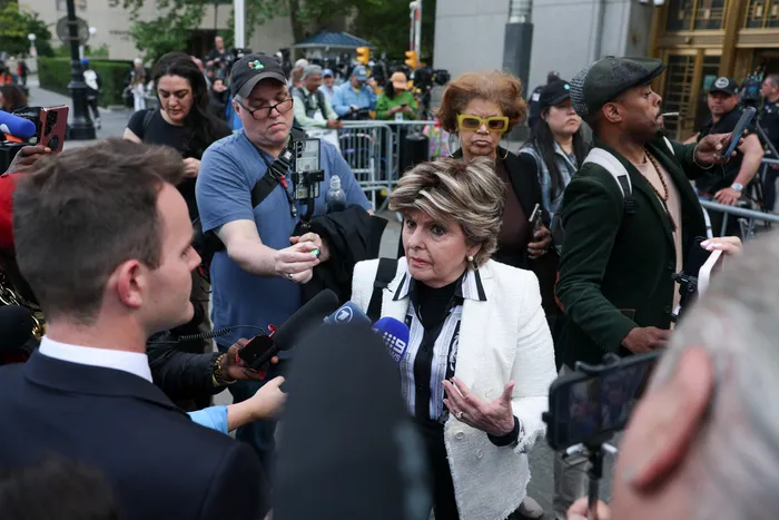 Gloria Allred speaking to reporters during a press conference surrounded by media personnel.