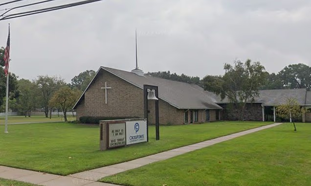 Exterior view of a church building featuring a cross and a sign in front.