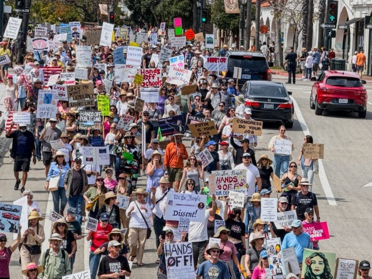 Crowd of people participating in a rally holding various protest signs on a city street.