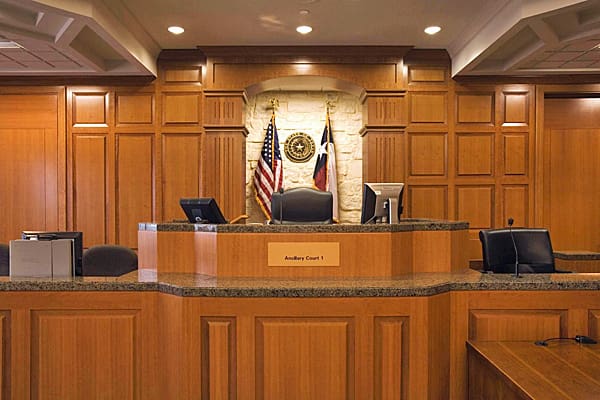 Interior view of a courtroom featuring a judge's bench with flags and a nameplate.