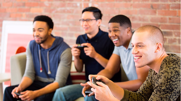 Four men engaged in playing video games together, smiling and holding controllers.