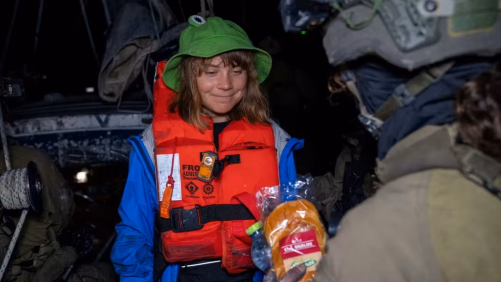 Greta Thunberg wearing a life jacket and a green hat while receiving a package.