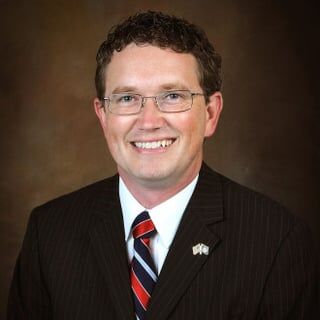 Portrait of Thomas Massie, a man wearing glasses and a suit with a striped tie.