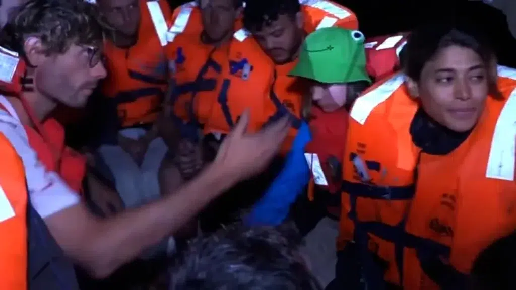 A group of individuals wearing orange life jackets, including Rima Hassan, gathered together in a close setting.