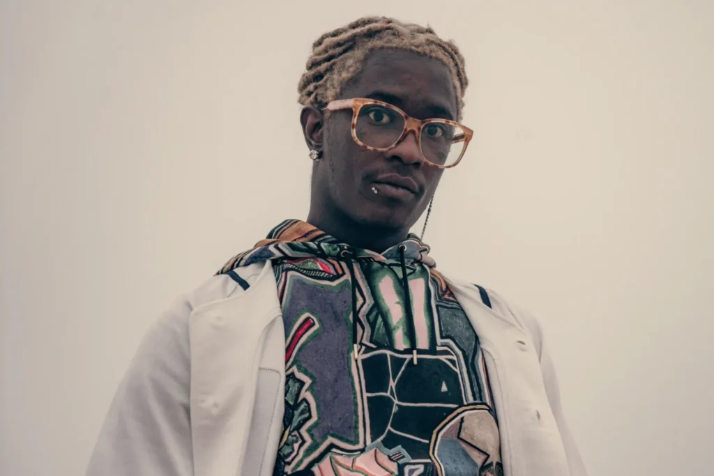 Portrait of Young Thug wearing a colorful hoodie and glasses.