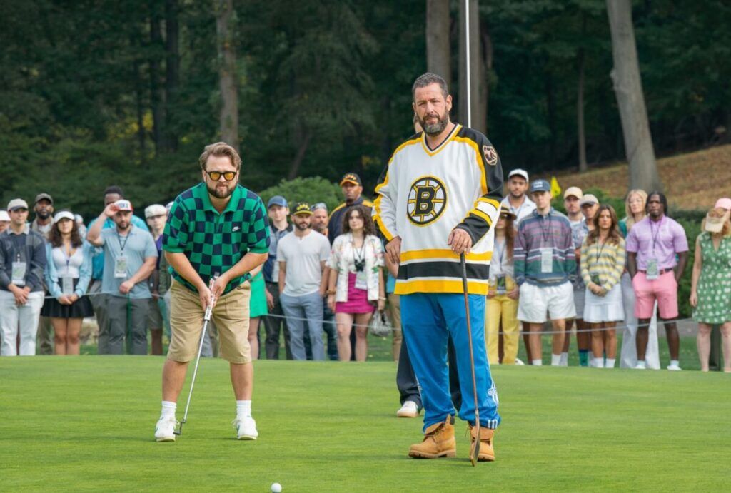 Two male golfers on a green with spectators watching in the background during a golf event.