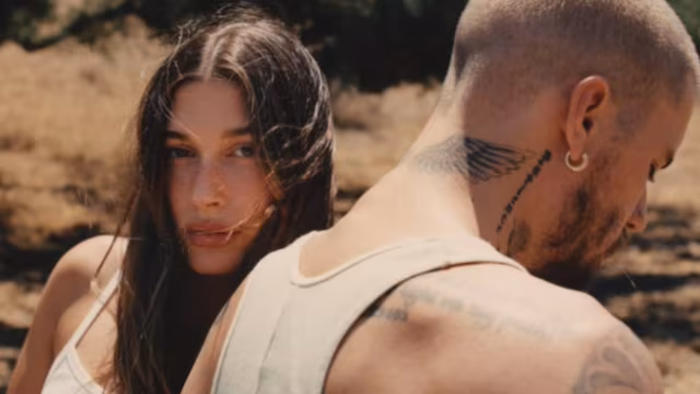 Justin Bieber- A couple standing close together, with the woman looking at the camera and the man facing away, displaying tattoos.