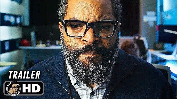A man with glasses and a beard displaying a serious expression in an indoor setting.