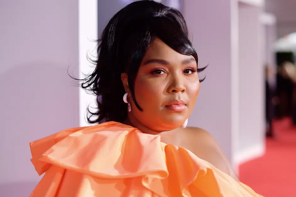 Lizzo posing for a photo at the 2019 American Music Awards wearing an orange dress.