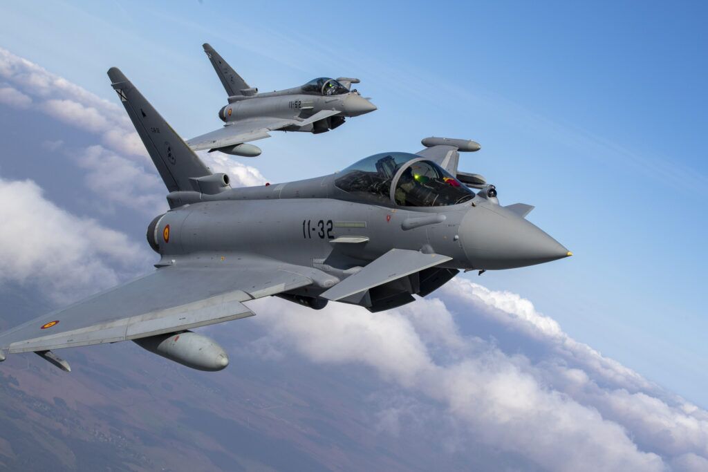 Two military fighter jets flying in formation against a blue sky with clouds.