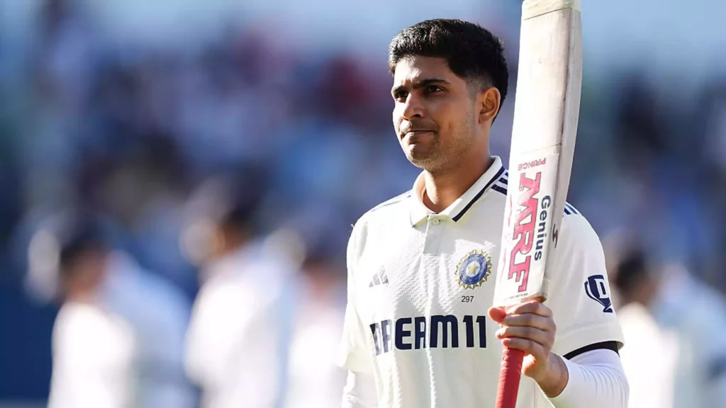 Shubman Gill standing on the cricket field holding a bat, wearing a white cricket uniform.