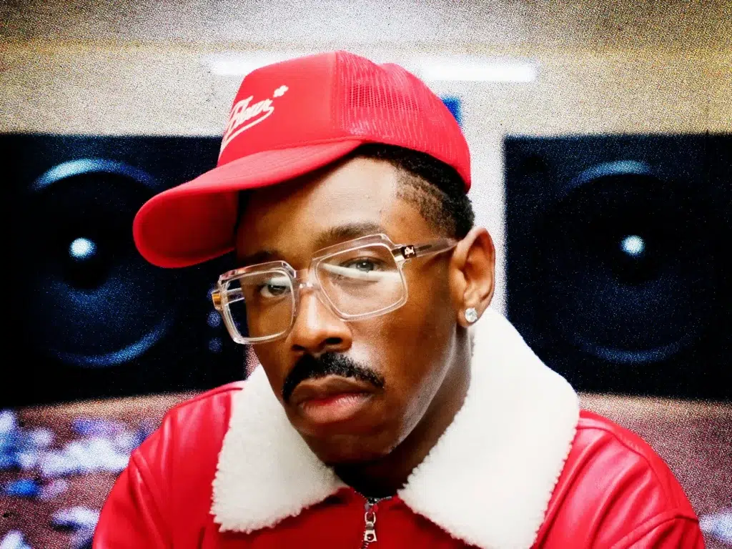 A man wearing a red jacket and cap, with glasses and a mustache, posing for the camera.