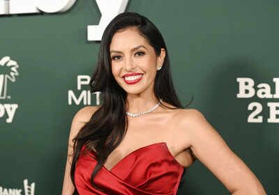Woman wearing a red dress and necklace, smiling at a formal event with a green backdrop.