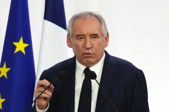 François Bayrou speaking at a podium with French and European Union flags in the background.