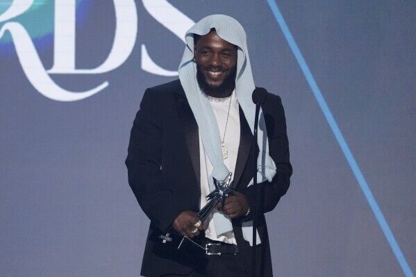 Kendrick Lamar smiling while holding an award on stage during an event.