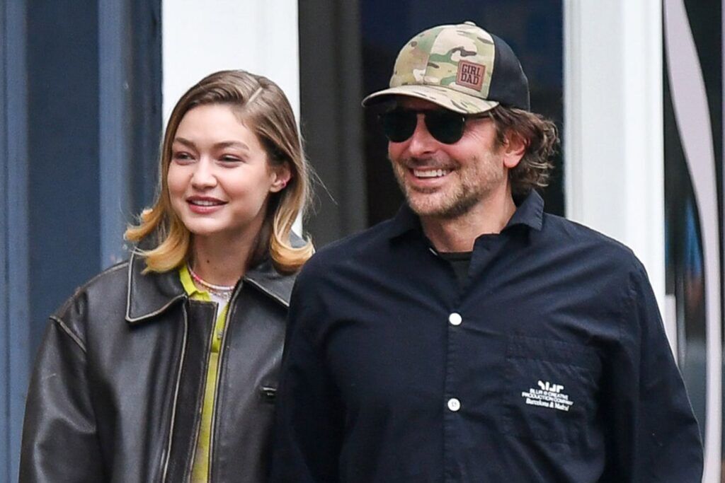 Gigi Hadid and Bradley Cooper smiling while walking outdoors in casual attire.