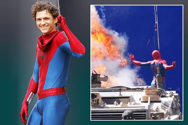 Tom Holland dressed as Spider-Man, posing on set with a blue background and flames in the distance.
