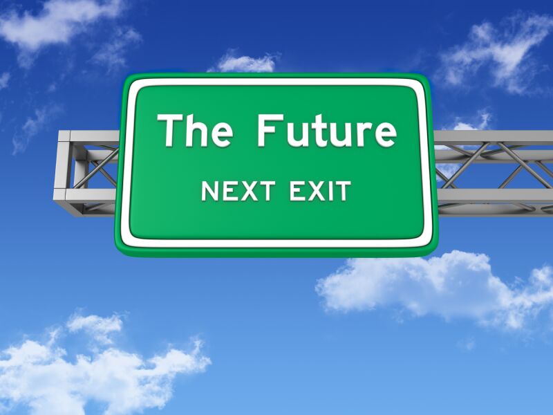 Green road sign that reads 'The Future' with 'NEXT EXIT' below it against a blue sky with clouds.