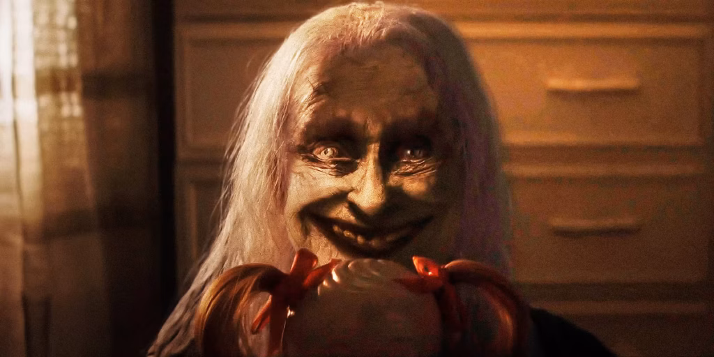 A figure with long white hair and a sinister smile holding a doll with red ribbons.