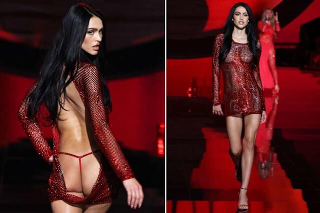 Model walking on a runway wearing a red sheer dress with a back cutout design.