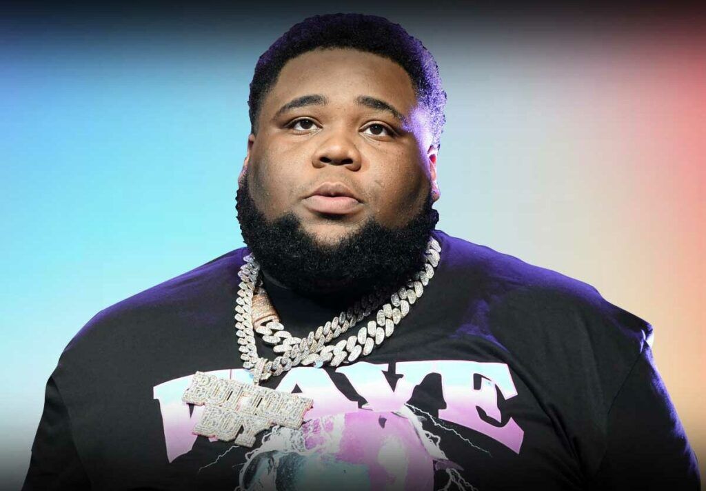 Rod Wave wearing a black shirt with the word 'WAVE' and a large chain necklace.