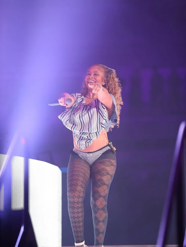 Jill Scott performing on stage with a microphone, wearing a striped top and fishnet stockings.